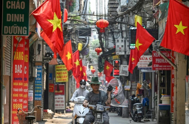 Un homme porte un ventilateur le long d'une rue bordée de drapeaux nationaux vietnamiens à Hanoï, le 30 avril 2024