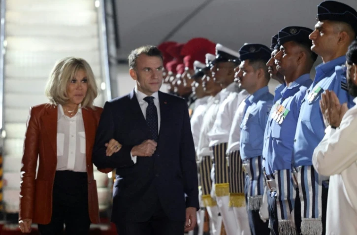 Le président français Emmanuel Macron (au centre à d.) et son épouse Brigitte Macron (à g.) sont accueillis par des responsables indiens à leur arrivée à Bombay, en Inde, le 17 février 2026