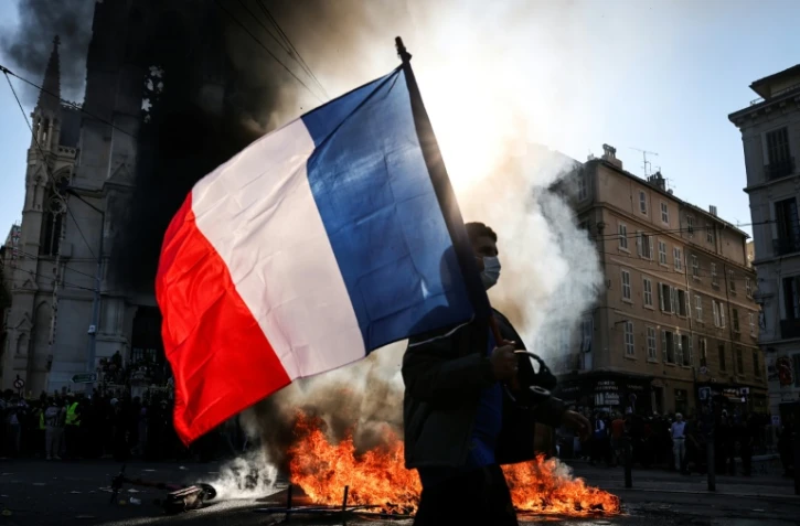 Un manifestant avec un drapeau français devant un feu, le 17 octobre 2026 à Marseille