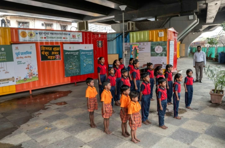 Des élèves chantent l'hymne national indien à "l'école du feu rouge" qui accueille des enfants défavorisés dans des conteneurs aménagés en salles de cours sous un pont autoroutier, le 18 mai 2026 à Bombay