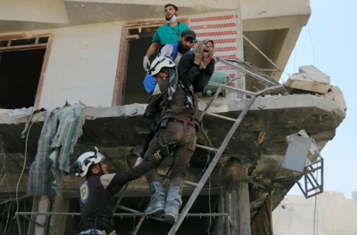 Des bénévoles du service de défense civil syrien évacuent des gens d'un immeuble détruit par des bombardements, dans un quartier rebelle d'Alep le 23 avril 2016