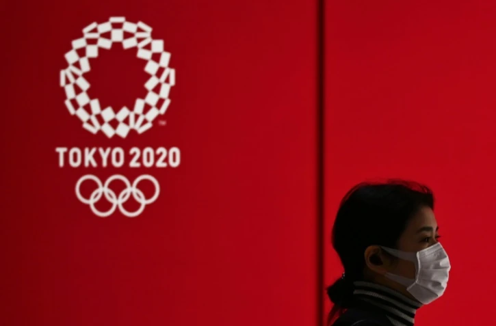 Une femme avec un masque passe devant le logo des JO de Tokyo de 2020 le 24 mars 2020 dans la capitale nippone.