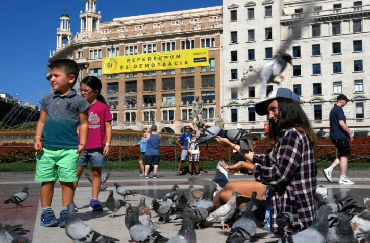 Sur cette photo prise le 13 septembre 2017 sur la place de Catalogne à Barcelone, une femme et des enfants nourrissent des pigeons devant une banderole "Oui. Le référendum c'est la démocratie" appelant à voter au référendum prévu le 1er octobre