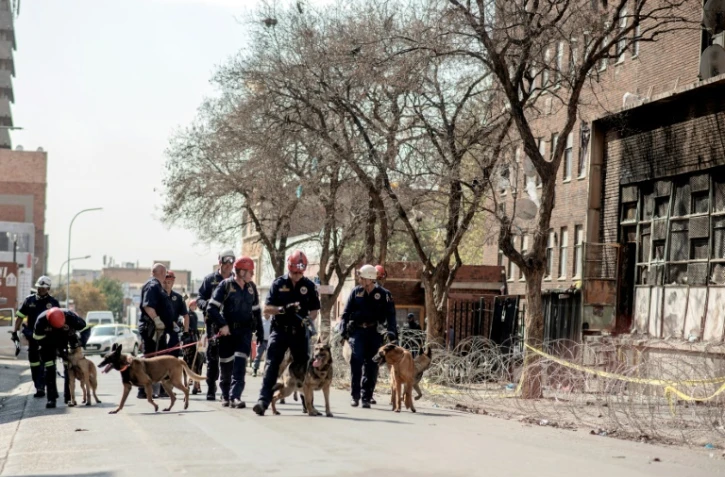 Des policiers de l'unité de recherche K-9 avec leurs chiens devant l'immeuble ravagé par un incendie, le 1er septembre 2023 à Johannesburg, en Afrique du Sud