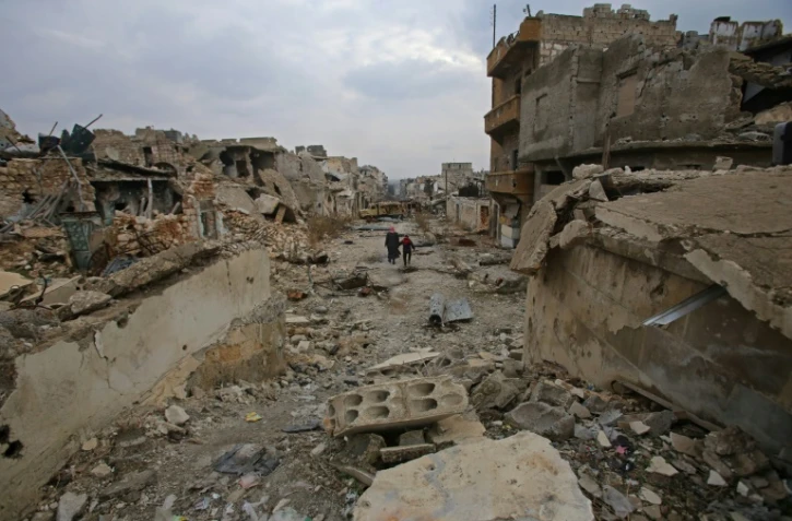 Des Syriens traversent une rue détruite du quartier al-Akroub d'Alep, le 17 décembre 2016
