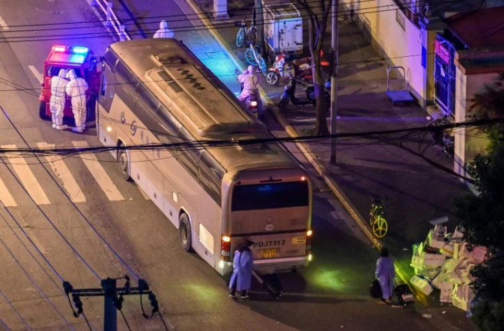 Des habitants de Shanghai avec des vêtements de protection et leur valise (en bas) attendent de monter dans un autocar, le 19 avril 2022