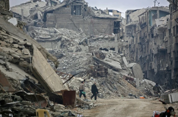 Des civils syriens marchent le long d'immeubles détruits par les bombardements du régime dans la ville rebelle, ancien fief rebelle dans la Ghouta orientale, le 30 mars 2018