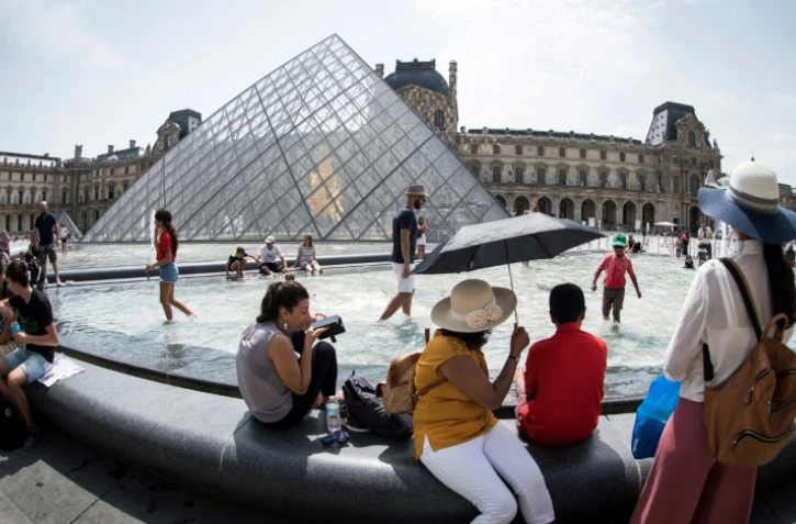 Touristes se rafraîchissant à la fontaine face à la pyramide du Louvre, à Paris le 7 août 2018