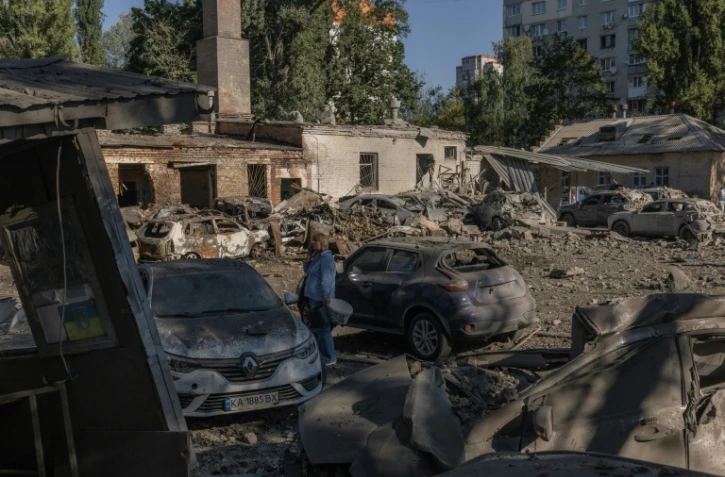 Une femme se tient près de voitures détruites et de bâtiments endommagés après une frappe russe à Kiev, le 20 août 2026
