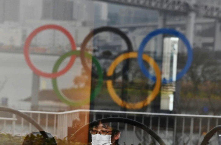 Les anneaux olympiques se réflétant sur une vitrine dans le parc de bord de mer d'Odaiba (baie de Tokyo) et un Japonais se protégeant du nouveau coronavirus avec un masque, le 8 mars 2020