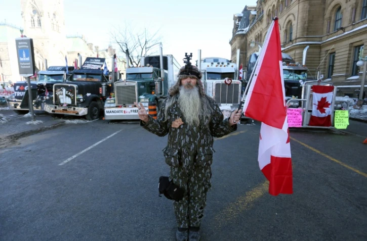 Un homme tient un drapeau du Canada près de la colline du Parlement où se trouvent des manifestants opposés aux mesures sanitaires, le 7 février 2022 à Ottawa