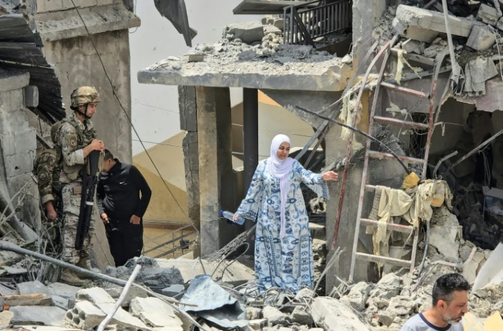 Une femme se fraye un chemin à travers les décombres sous le regard d'un soldat libanais, sur le site d'un immeuble résidentiel touché la veille par une frappe israélienne près de la ville de Burj al-Shamali, au sud de Tyr, le 27 mai 2026