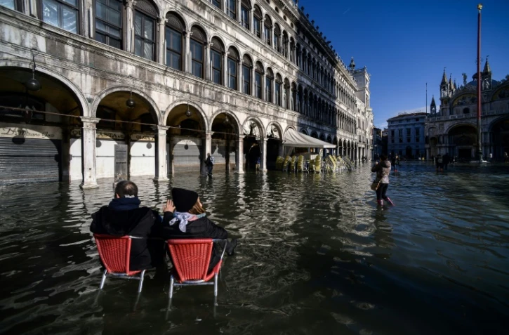 Un couple assis sur des chaises de café observe la place Saint-Marc inondée, à Venise le 14 novembre 2019