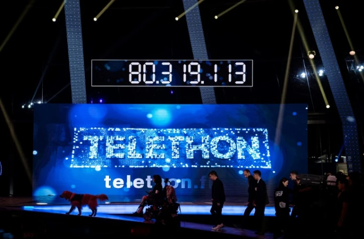 Des invités marchent devant le compteur de dons de l'édition 2016 du Téléthon, à Paris, le 4 décembre