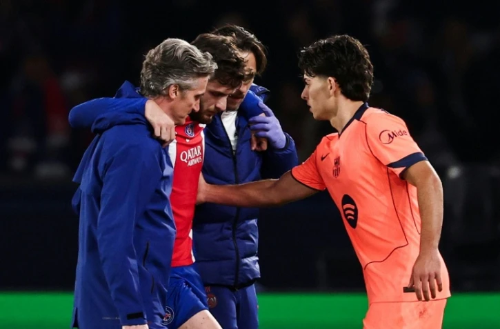 L'attaquant du PSG Khvicha Kvaratskhelia (c) quitte la pelouse après s'être blessé au genou droit lors du match contre le FC Barcelone, réconforté par Xavi Espart, le 20 octobre 2026 au Parc des Princes