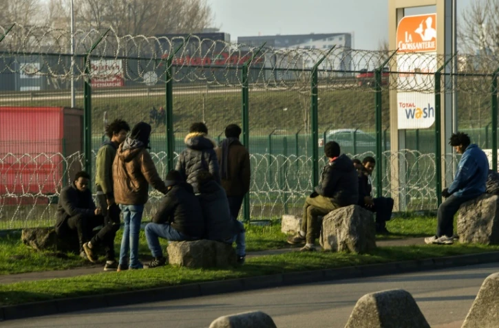 Des migrants derrière un grillage barbelé d'un parking pour camions près de la N216 conduisant au terminal de ferry, le 12 janvier 2018 à Calais 