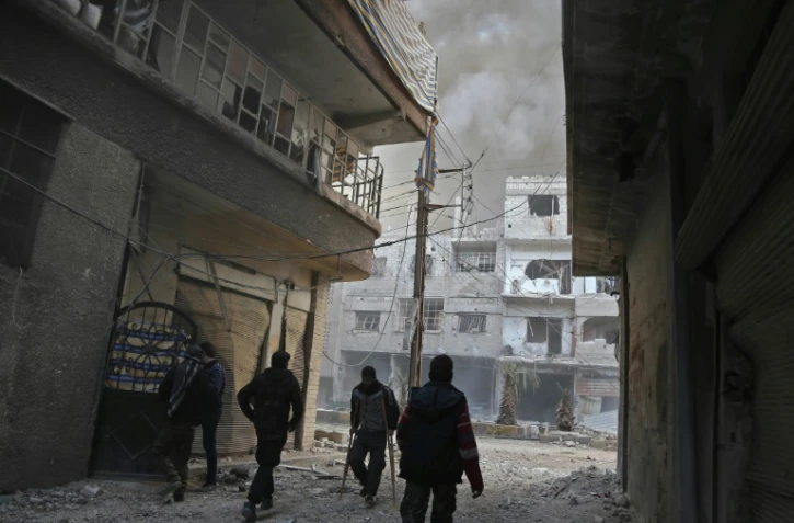 Des colonnes de fumée et de la poussière s'élèvent de la localité de Hammouriyé dans le fief rebelle de la Ghouta orientale près de Damas, après un raid du régime, le 21 février 2018