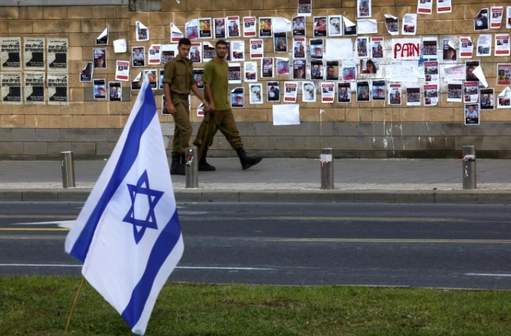 Des soldats passent devant un mur du ministère de la Défense à Tel Aviv, le 16 octobre, sur lequel des photos des Israéliens enlevés par le Hamas le 7 octobre 2023 ont été collées
