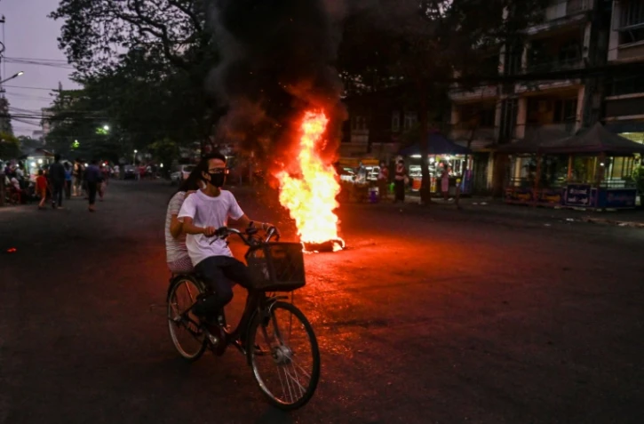 Un couple à vélo passe devant un feu allumé par les manifestants anti-junte à Rangoun, le 3 avril 2021