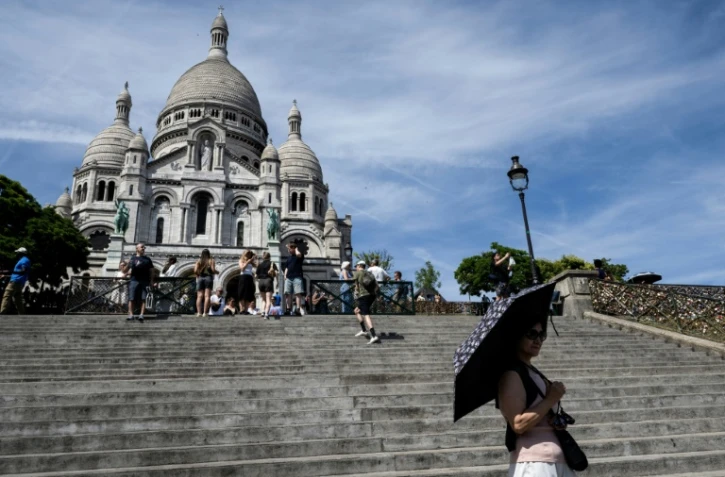 Une touriste se protège du soleil avec un parapluie devant la basilique du Sacré-Cœur à Paris, le 6 juillet 2026, lors d'une vague de chaleur en France