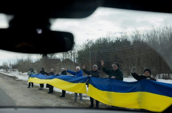 Des personnes tiennent un drapeau ukrainien le long d'une route pour accueillir un convoi de soldats libérés par les Russes après un échange de prisonniers, le 6 mars 2026 dans un lieu non précisé dans le nord de l'Ukraine