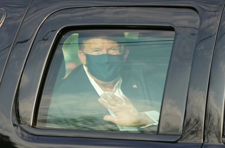 Le président américain Donald Trump salue ses symathisants depuis la limousine présidentielle lors d'une brève sortie de l'hôpital militaire de Walter Reed à Bethesda, près de Washington, le 4 octobre 2020                    