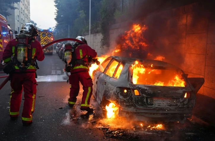 Des pompiers tentent d'éteindre une voiture en feu en marge d'une manifestation à Nanterre,  théâtre d'incidents en soirée, le 27 juin 2023