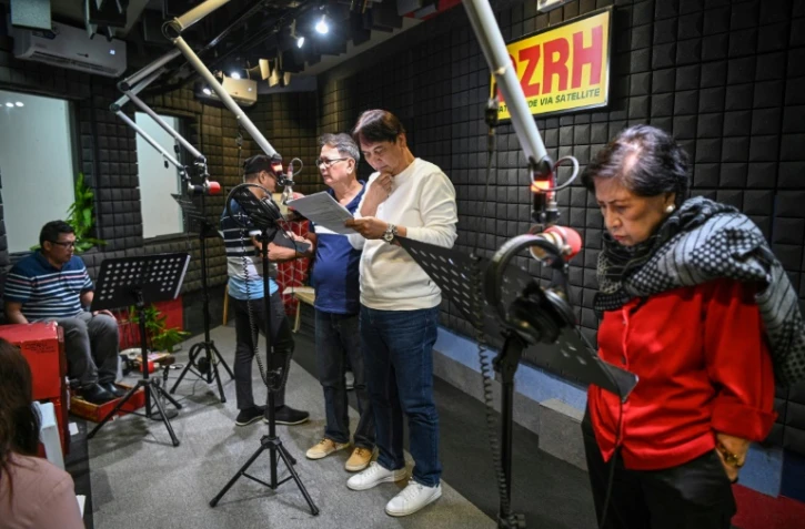 Le comédien Phil Cruz (3e g), son frère Robert (2e d) et d'autres comédiens enregistrent leurs rôles pour un feuilleton radiophonique dans le studio d'une station de radio à Manille, le 17 juillet 2023 aux Philippines