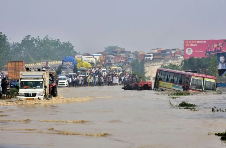 Des personnes se tiennent sur un pont aérien sur une route nationale inondée après le débordement de la rivière Kosi suite à de fortes pluies près de Rampur dans l'État indien de l'Uttar Pradesh, le 20 octobre 2021