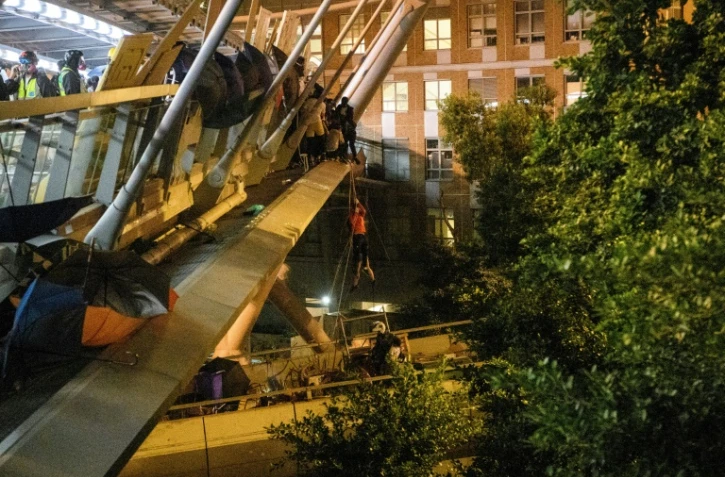 A protester (C) lowers herself down a rope from a bridge to a highway to escape from the campus of Hong Kong Polytechnic University