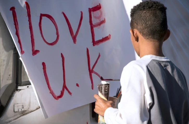 Un jeune migrant réalise une pancarte, "j'aime le Royaume-Uni", à Calais le 31 octobre 2016