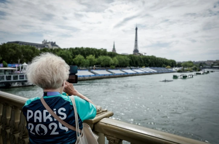 Une bénévole des JO-2024 prend une photo sur le pont des Invalides à côté des tribunes installées sur la Seine à la veille de la cérémonie d'ouverture des Jeux Olympiques 2024, à Paris, le 25 juillet 2024