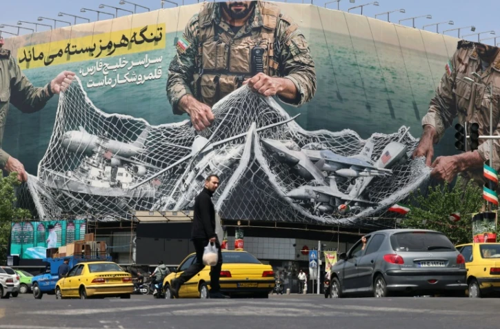 Des véhicules passent devant un panneau d'affichage géant portant l'inscription: "Le détroit d'Ormuz reste fermé"  sur la place de la Révolution à Téhéran, le 28 avril 2026