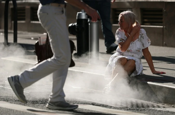 Une touriste assise à côté de la vapeur d'eau sortant d'une bouche d'aération dans le quartier de Wall Street, à New York, alors qu'une alerte à la chaleur extrême a été émise, le 23 juin 2025
