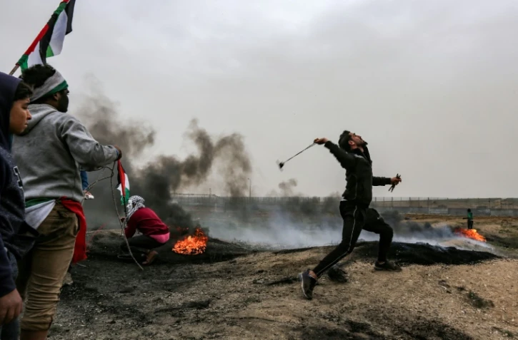 Un Palestinien lance une pierre en direction des soldats israéliens postés de l'autre côté de la barrière frontalière entre la bande de Gaza et Israël, lors du premier anniversaire des "Grandes marches du retour", le 30 mars 2019 à l'est de Gaza city
