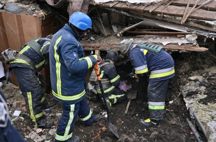 Des membres des services de secours cherchent dans les décombres d'un immeuble, le 8 janvier 2024 à Zmiiv, dans la région de Kharkiv, en Ukraine