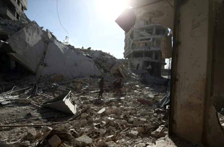 Des Syriens au milieu des destructions dans la localité de Saqba, dans l'enclave rebelle de la Ghouta orientale, bombardée par le régime syrien, le 9 mars 2018 