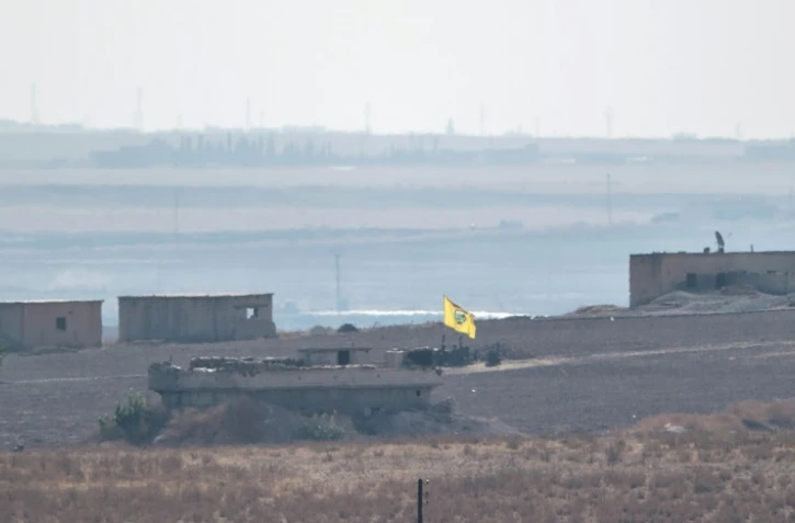 Photo prise depuis le côté turc de la frontière turco-syrienne, montrant un drapeau des Unités de protection du peuple (YPG) flottant au-dessus d'un bâtiment près de la ville syrienne de Tal Abyad, le 8 octobre 2019