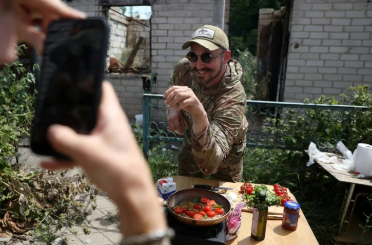 Ukrainian serviceman and influencer Ruslan Mokrytskyi poses for the camera as he cooks pasta as his fellow soldier records a video of him for Tik Tok in an undisclosed location in the Donetsk region, on July 27, 2024, amid the Russian invasion in Ukraine. At the front since the start of the war in 2022, Mokrytskyi needed a form of escape while being under constant fire. "After missions, there were, let's say... many horrible and stressful images," he said, hesitantly. "I needed to recuperate mentally." He tried to forget the horrors by plunging into films, music, reading, going on walks despite the bombs. But nothing worked. "I got to the point where I told myself that it would be cool to film myself making fries for instance," the soldier said. The success of that idea exceeded his expectations: his fries video got three million views. Encouraged, Mokrytskyi involved friends from his battalion, who would call their wives to get ideas for recipes. He then realised he was not only helping his own mental health bRouslan Mokrytsky, soldat et influenceur ukrainien le 25 juillet 2024 dans la région de Donetsk