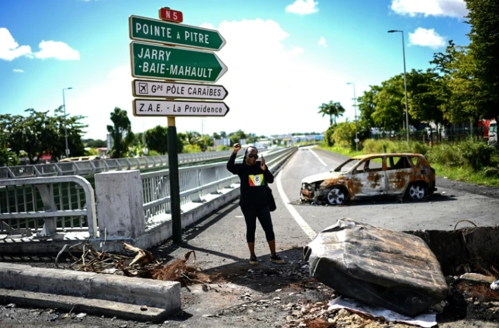 Une manifestante portant un t-shirt aux couleurs de l'UGTG (Union générale des travailleurs de Guadeloupe) lève le poing devant du matériel brûlé aux Abymes, près de Pointe-à-Pitre en Guadeloupe, le 24 novembre 2021