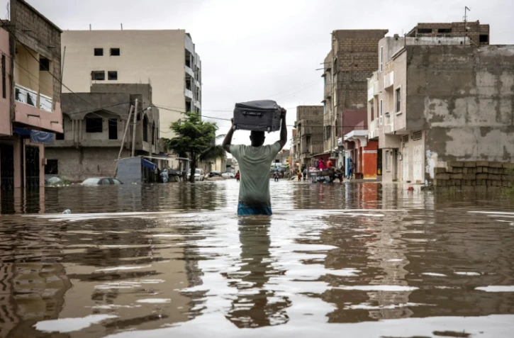 Un homme porte une valise sur sa tête en traversant une rue inondée de Dakar, au Sénégal, le 20 août 2021