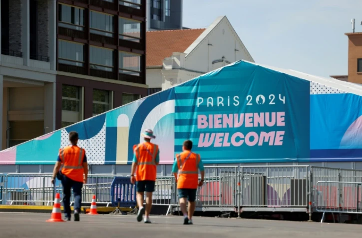 Des membres de l'organisation des JO-2024 marchent près de l'entrée du village des athlètes, le 18 juillet 2024 à Saint-Denis en Seine-Saint-Denis