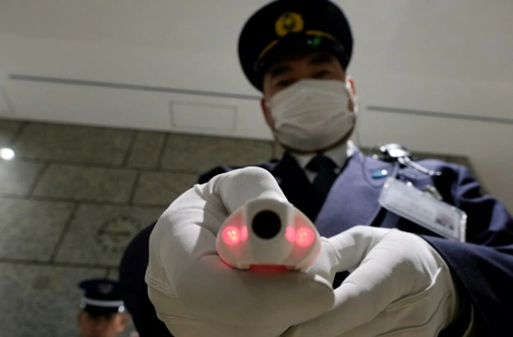 Un agent de sécurité montre un appareil de mesure de la température corporelle, à la réception d'un bâtiment officiel de Tokyo le 5 mars 2020