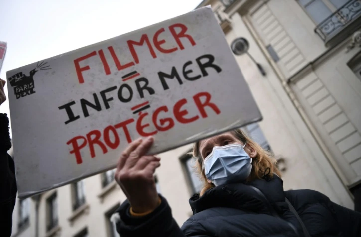 Une manifestante tient une pancarte "filmer = informer = protéger" durant une manifestation contre la loi sécurité globale devant le Sénat le 16 mars 2021