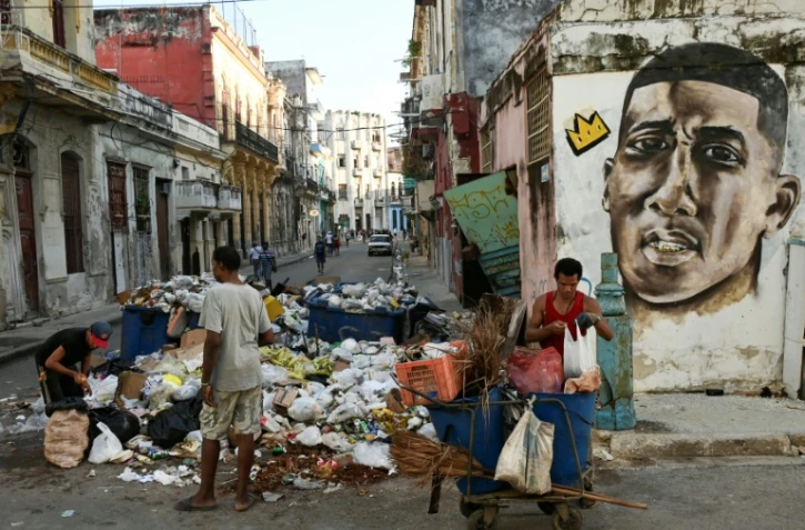 Des Cubains devant un tas d'ordures dans une rue de La Havane, le 23 août 2024