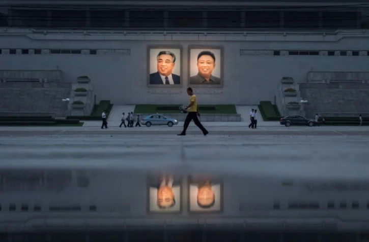 Des passants et des véhicules passent devant les portraits des derniers dirigeants nord-coréens Kim Il-Sung (à gauche) et Kim Jong-Il (à droite), le 21 juillet 2017, à Pyongyang. 