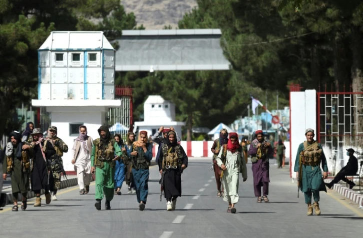 Des combattants talibans marchent devant la principale entrée de l'aéroport de Kaboul, le 28 août 2021