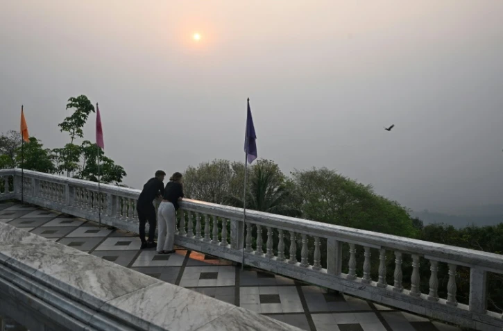 Des touristes face à une vue sur Chiang Mai, obscurcie par la pollution, depuis le sommet du temple Wat Phra That Doi, le 15 mars 2024 en Thaïlande