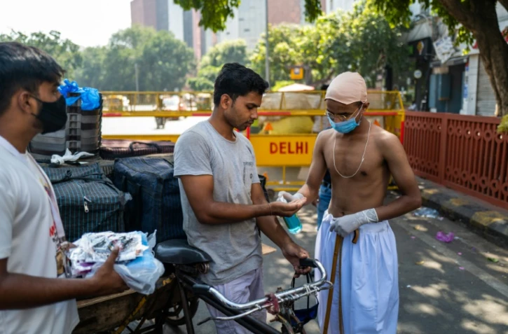 Des bénévoles, dont un habillé comme le héros de l'indépendance indienne, le Mahatma Gandhi, dont c'est l'anniversaire, distribuent des masques aux conducteurs de vélos-taxis, à New Delhi le 2 octobre 2020