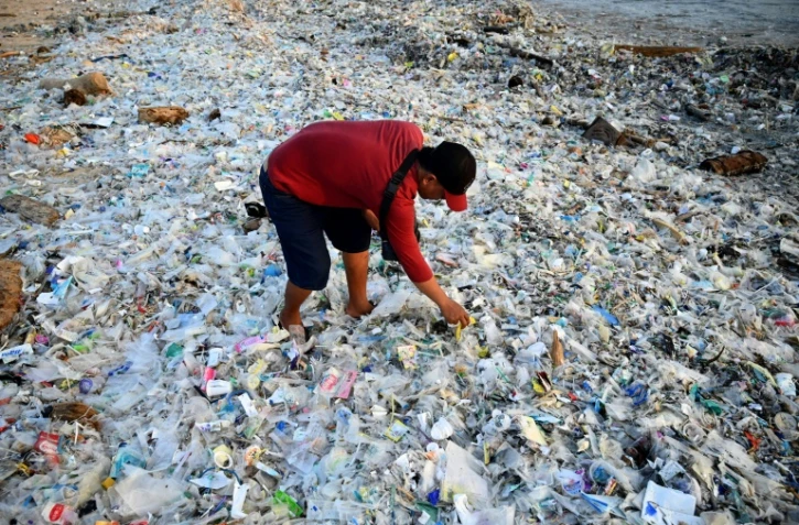 Un homme fouille dans des ordures et déchets plastiques échoués sur la plage de Kedonganan, sur l'île indonésienne de Bali, le 19 mars 2024